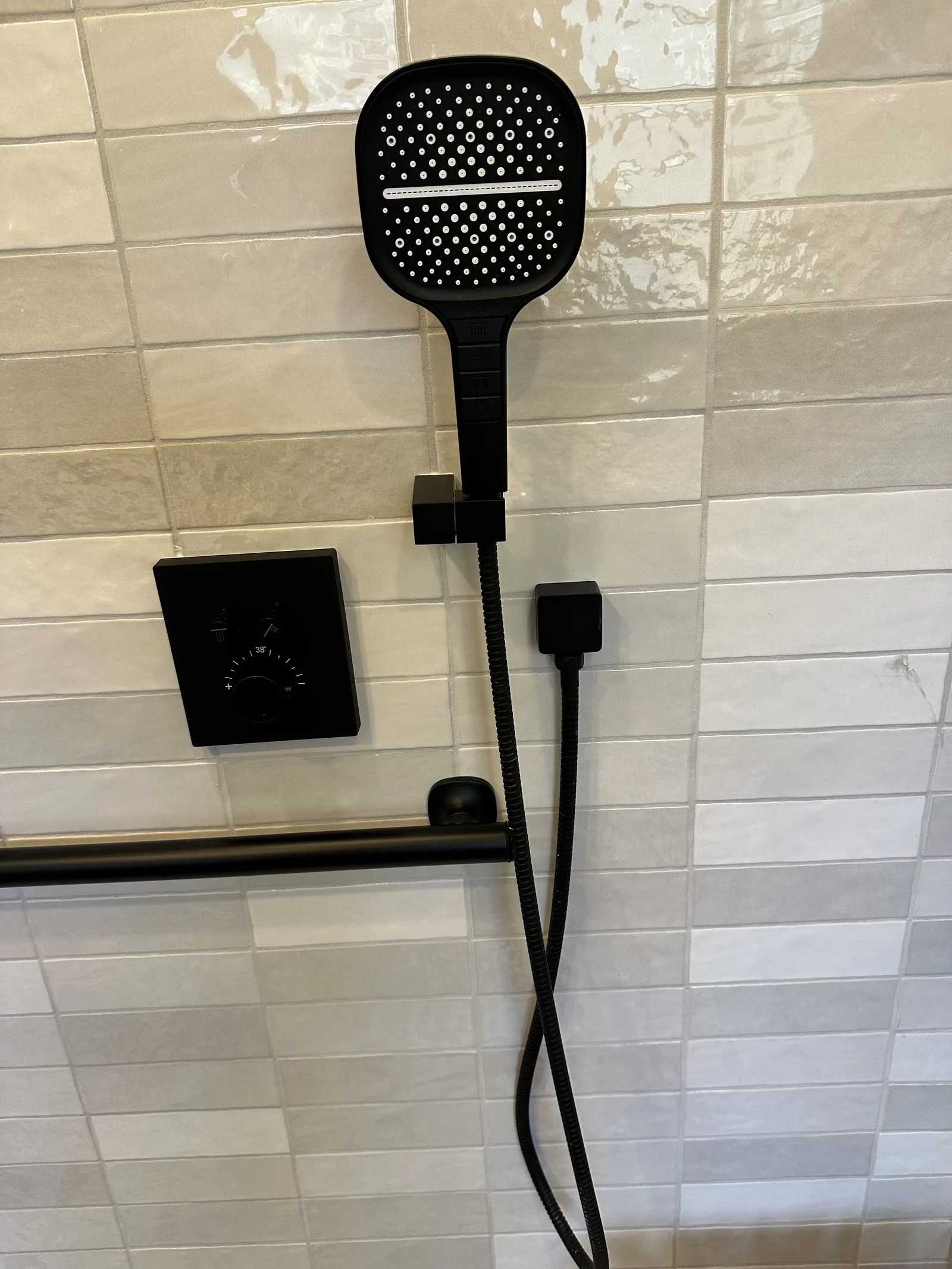 Black handheld shower head on a slide bar above a grab bar on white tile in a Houston accessible bathroom remodel
